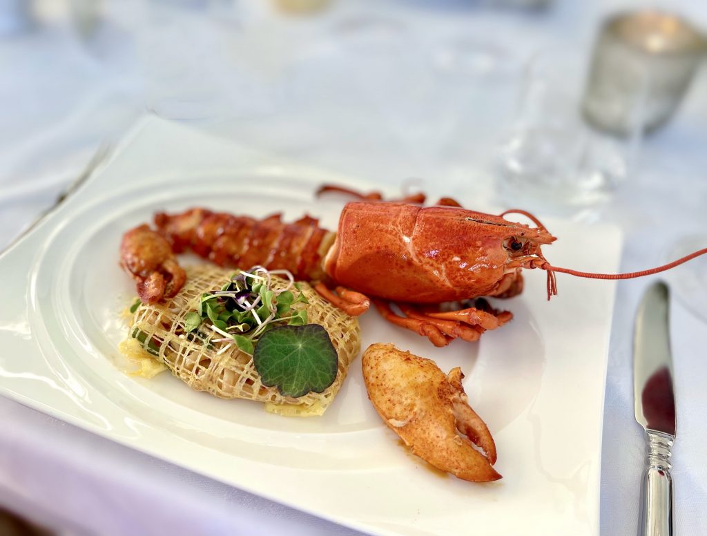 A dish with lobster and a dumpling that looks like a small cage, garnished with greens